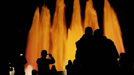 siluetas de personas que admiran la fuente alta con luces en barcelona
