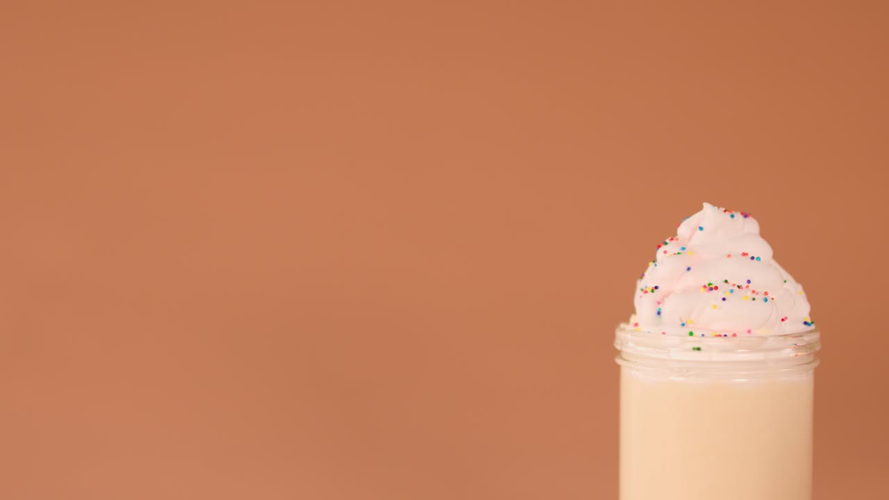 Una mano umana decora un cremoso milkshake con biscotti e cannuccia su uno sfondo caldo da studio