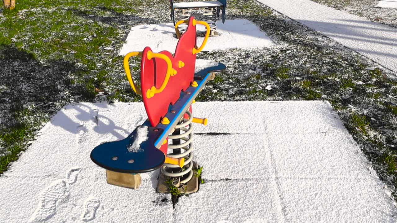 Gorgous and fun vibrant colored spring rider bouncing and wobbling back and fourth at a winter sunny playground with fresh white snow covering it. Green grass still visible from late autumn