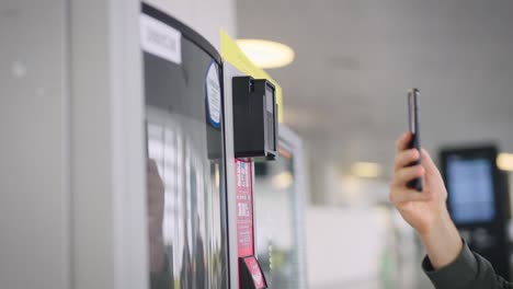 en el marco, la mano de un hombre con un teléfono inteligente y una máquina expendedora. el hombre paga por su café y bocadillos
