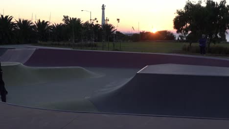 toma en cámara lenta de un niño moliendo en un riel en un parque de patinaje patinando durante la puesta de sol