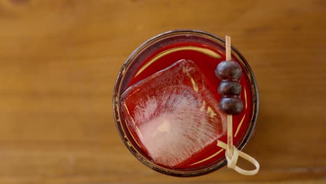 Overhead-Video-Einer-Aufnahme-Von-Beeren-Mit-Gin-Und-Blaubeeren,-Serviert-In-Einem-Glas-Mit-Eiswürfeln-Auf-Einem-Holztisch