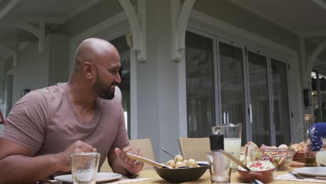 happy biracial parents and daughter serving meal at dinner table in garden, slow motion