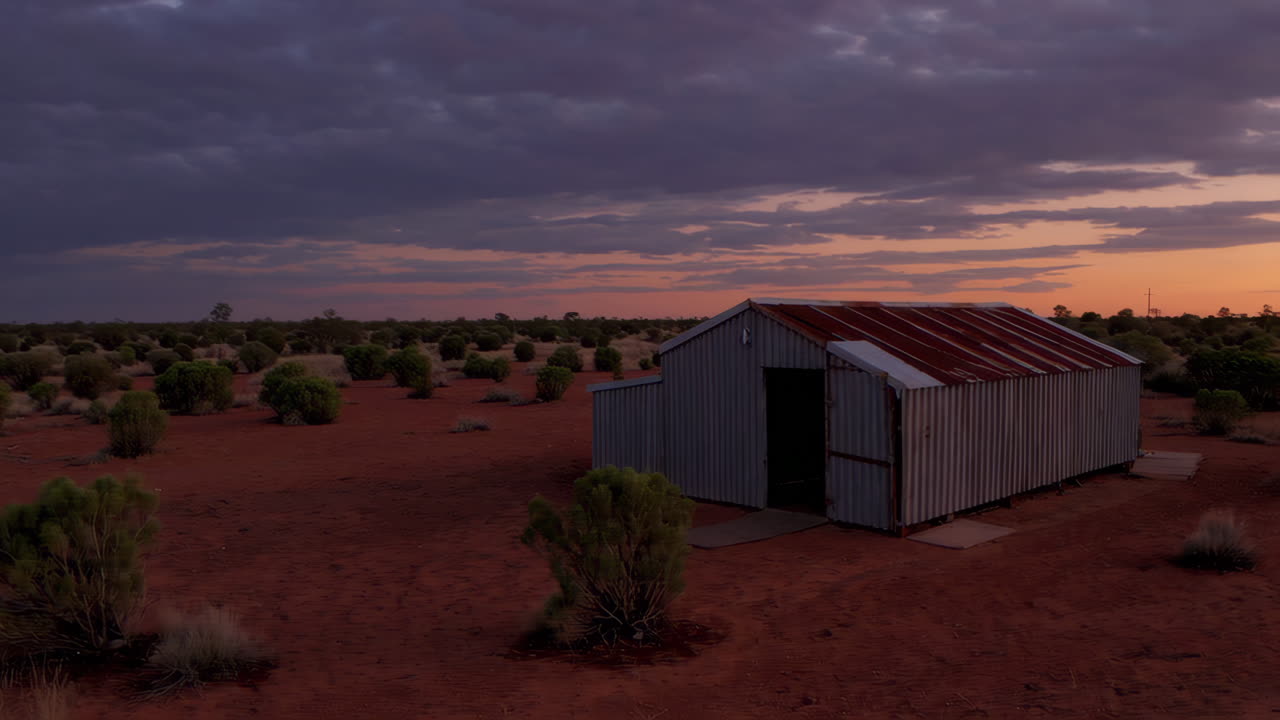 Remote corrugated iron shed in a red desert landscape at dusk