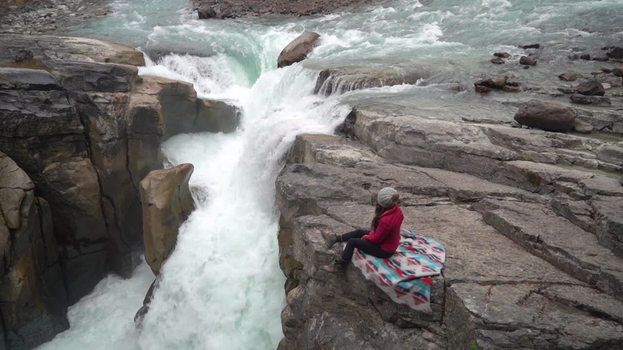 mujer sentada en una roca sobre una cascada y un río glacial en el campo canadiense en un frío día de otoño