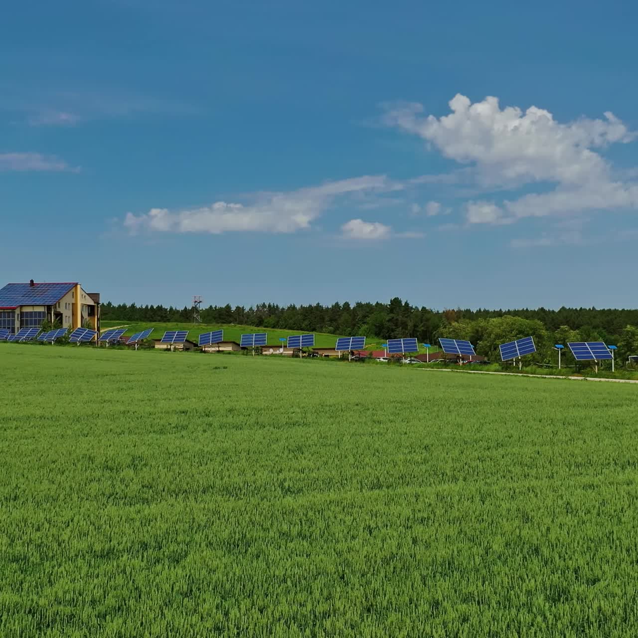 Green field in spring. Solar photovoltaic panels on the modern complex among beautiful nature landscape. Drone flight. Camera moves forward.