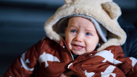 man holding a little kid wearing warm brown and white jacket. mother wants to kiss a baby and he gets nervous.