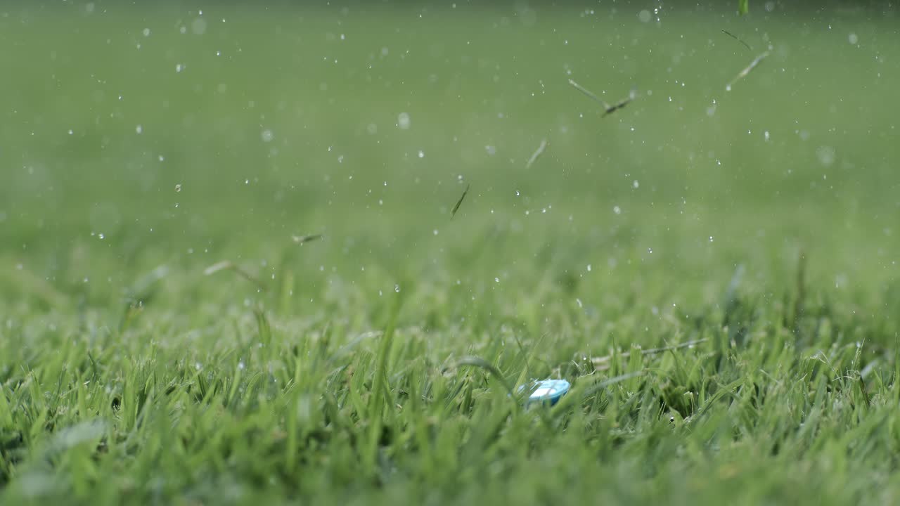 Una mazza da golf colpisce una pallina da golf bianca al rallentatore. Gocce di rugiada mattutina e particelle d'erba si sollevano in aria dopo l'impatto. Scatto realizzato con una telecamera al rallentatore a 1.000 fps.