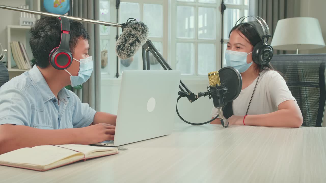 Wearing Protect Mask, Asian Boy Host Record Podcast Use Microphone Wear Headphone With Laptop Interview Guest Conversation For Content In His Home Studio. Content Creator Concept