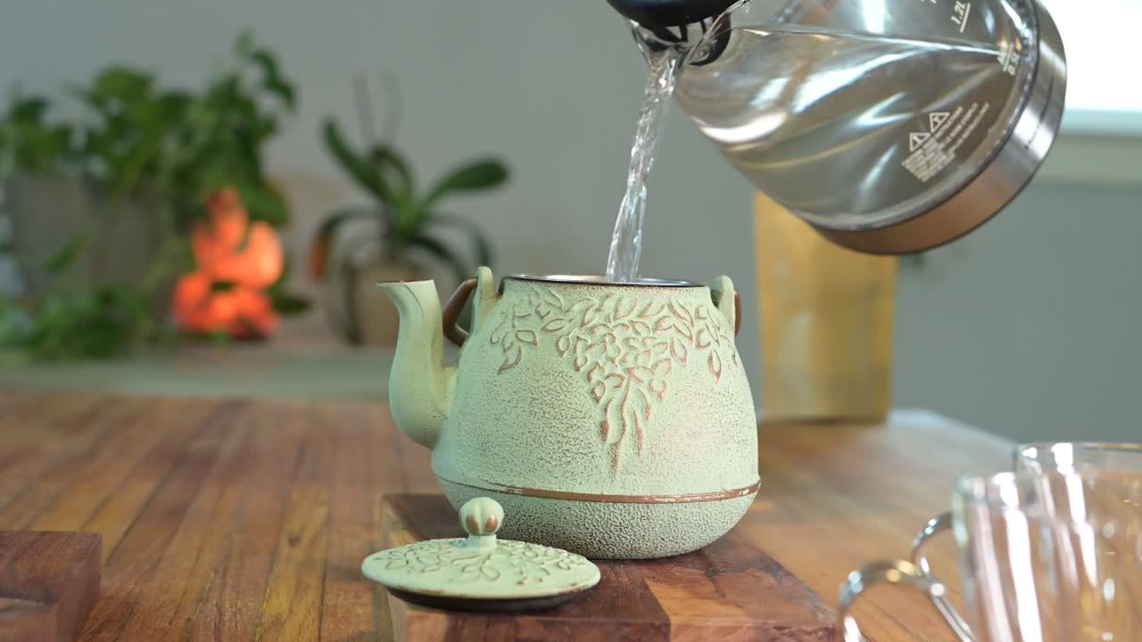 hacer té de hierbas en una tetera verde sobre una mesa de madera en una habitación luminosa y aireada con plantas verdes en el fondo y una taza de té de vidrio