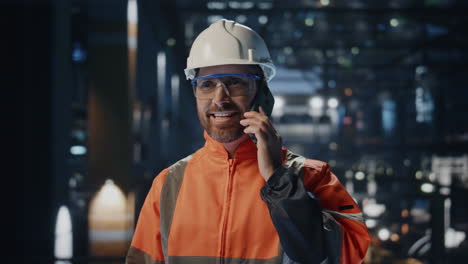un mecánico de fábrica alegre hablando por teléfono móvil en la producción de cerca. trabajador feliz