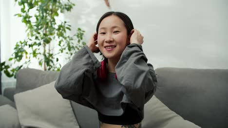 Portrait-of-gentle-asian-lady-wearing-wireless-headphones,-sitting-on-couch-and-smilling
