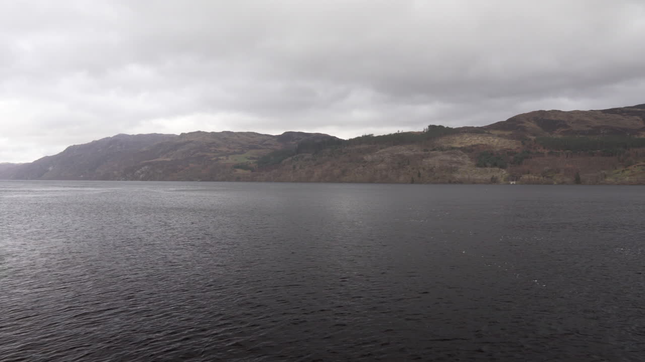 Panning shot from the coast of Loch Ness on the lake and surrounding mountains on a cloudy day in Scotland
