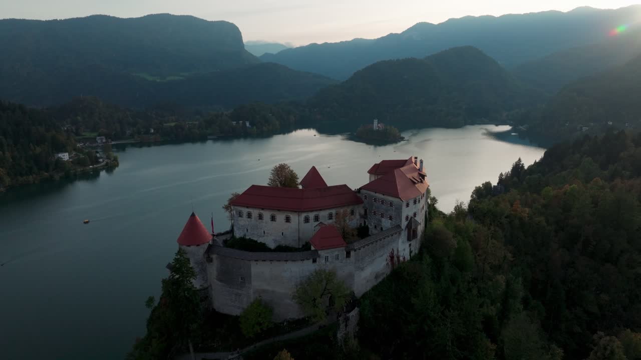 Castello di Bled arroccato sopra il Lago di Bled con montagne nella morbida luce del mattino, panoramica aerea