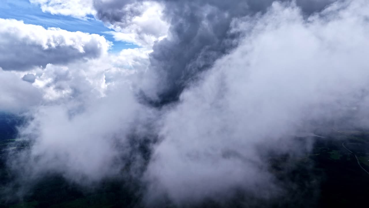A stunning, immersive aerial drone shot flies close to and through majestic white and grey clouds, revealing the vast green forest landscape of Latvia below