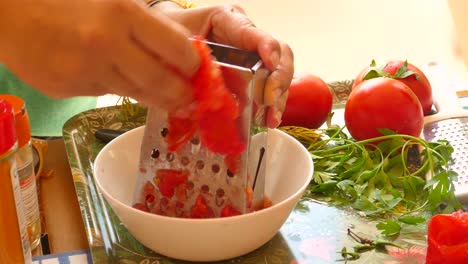 close up shot of hands holding the grater and grating tomato into small pieces for paella sauce preparation called sofrito in a kitchen