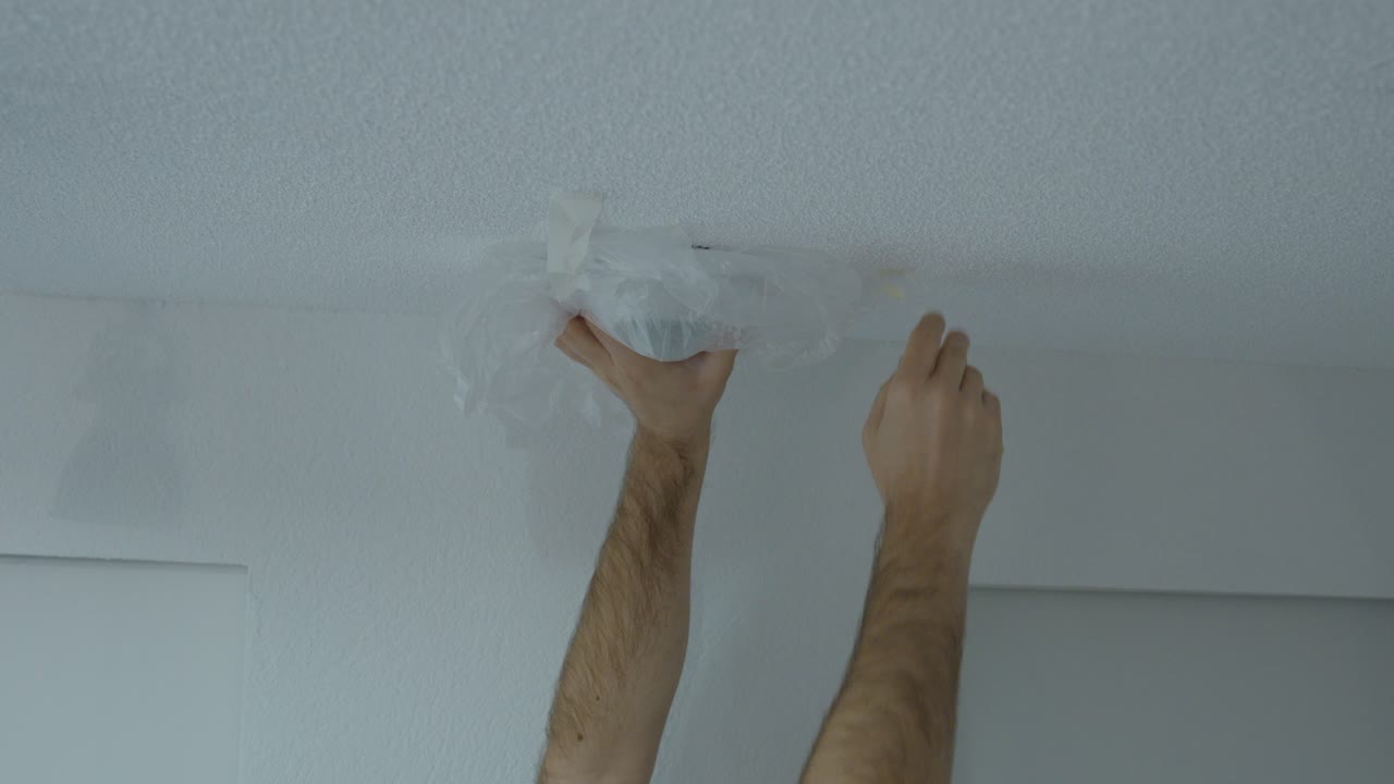 Primo piano di una persona che applica un sacchetto di plastica su un rilevatore di fumo a soffitto, illustrando pericolose violazioni della sicurezza antincendio, manomissione dell'allarme e comportamenti a rischio domestico