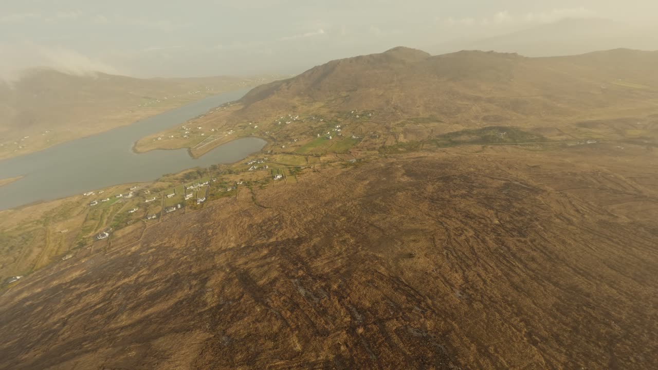 avión no tripulado buceando a través de las nubes sobre la isla de achill, irlanda hacia un pequeño pueblo junto al océano atlántico durante la puesta de sol