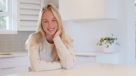 Smiling woman at home adjusting hair in bright kitchen setting, copy space