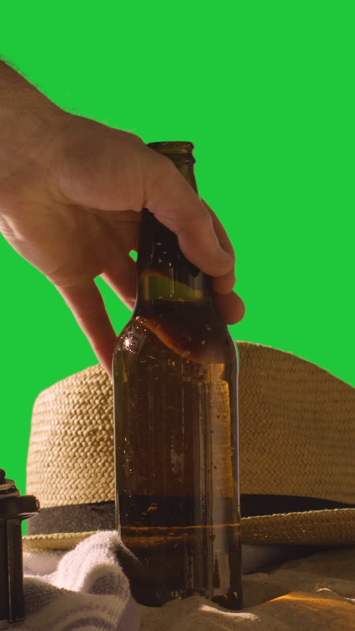 concepto de vacaciones de verano vertical de botella de cerveza en la toalla de playa con y sombrero de sol contra la pantalla verde 1