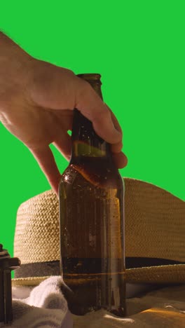 Vertikales-Video-Sommerferienkonzept-Der-Bierflasche-Auf-Strandtuch-Mit-Sonnenhut-Vor-Grünem-Bildschirm-1