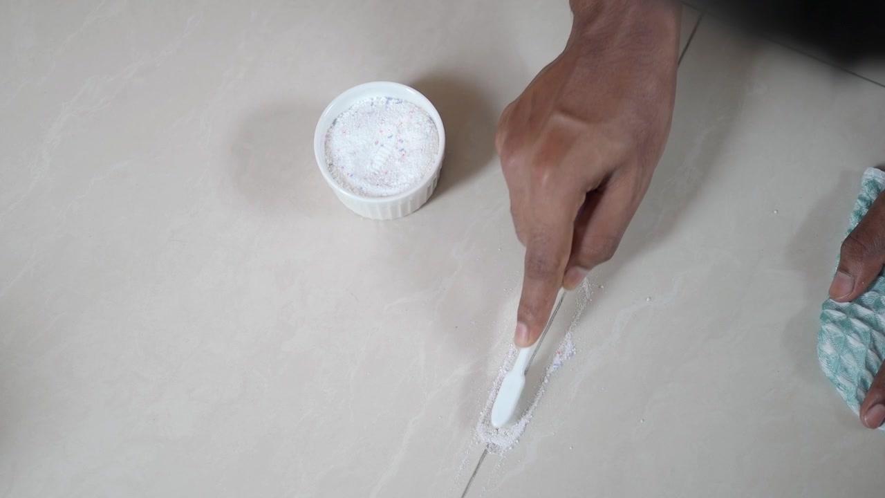 Persona limpiando la lechada de los azulejos con un cepillo de dientes y polvo limpiador