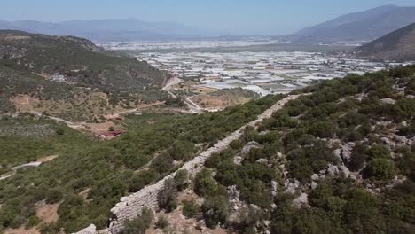 drone panning from the bottom going up, showing the wall along the lycian way's hiking trail and a modern turkish town in antalya province in turkey