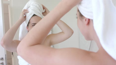 happy caucasian woman looking in front of mirror with towel on head in bathroom in slow motion