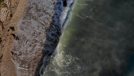 sea waves foaming and splashing on pebbles beach down the rocky hill in mediterranean