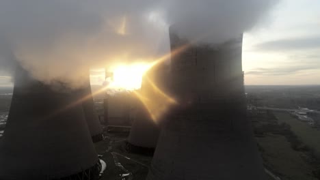 Aerial-view-of-UK-power-station,-sunrise-heading-behind-cooling-towers,-smoke-steam-emissions,-global-warming