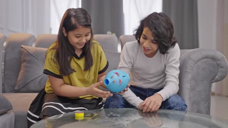 happy indian siblings taking out money from piggy bank