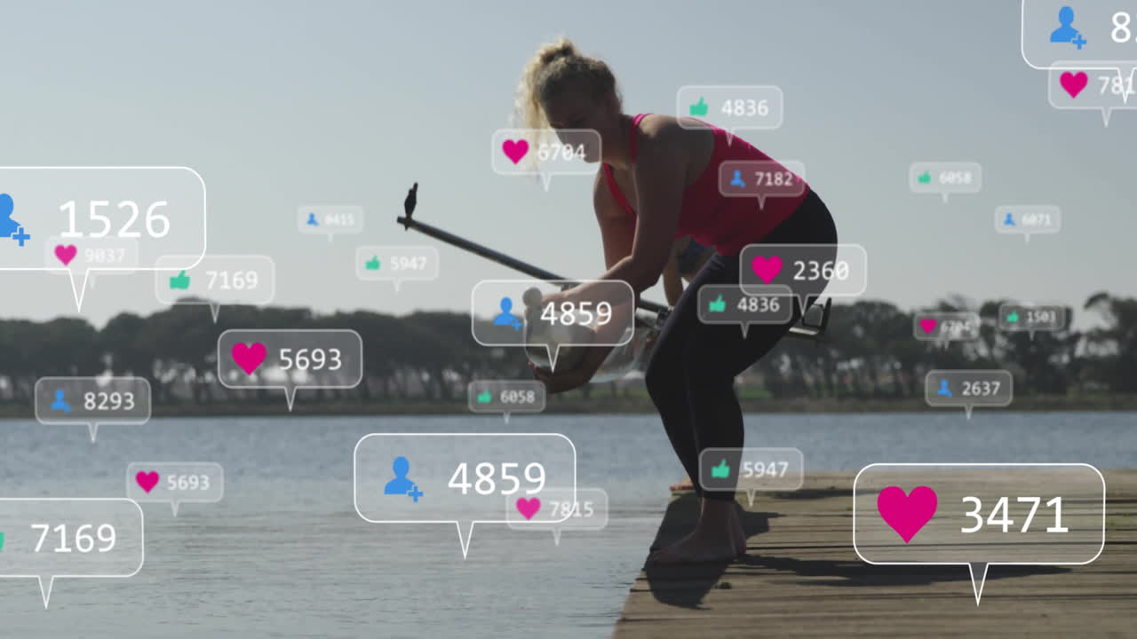 Woman kneeling on wooden dock grabbing paddle at lake showing floating fitness media icons