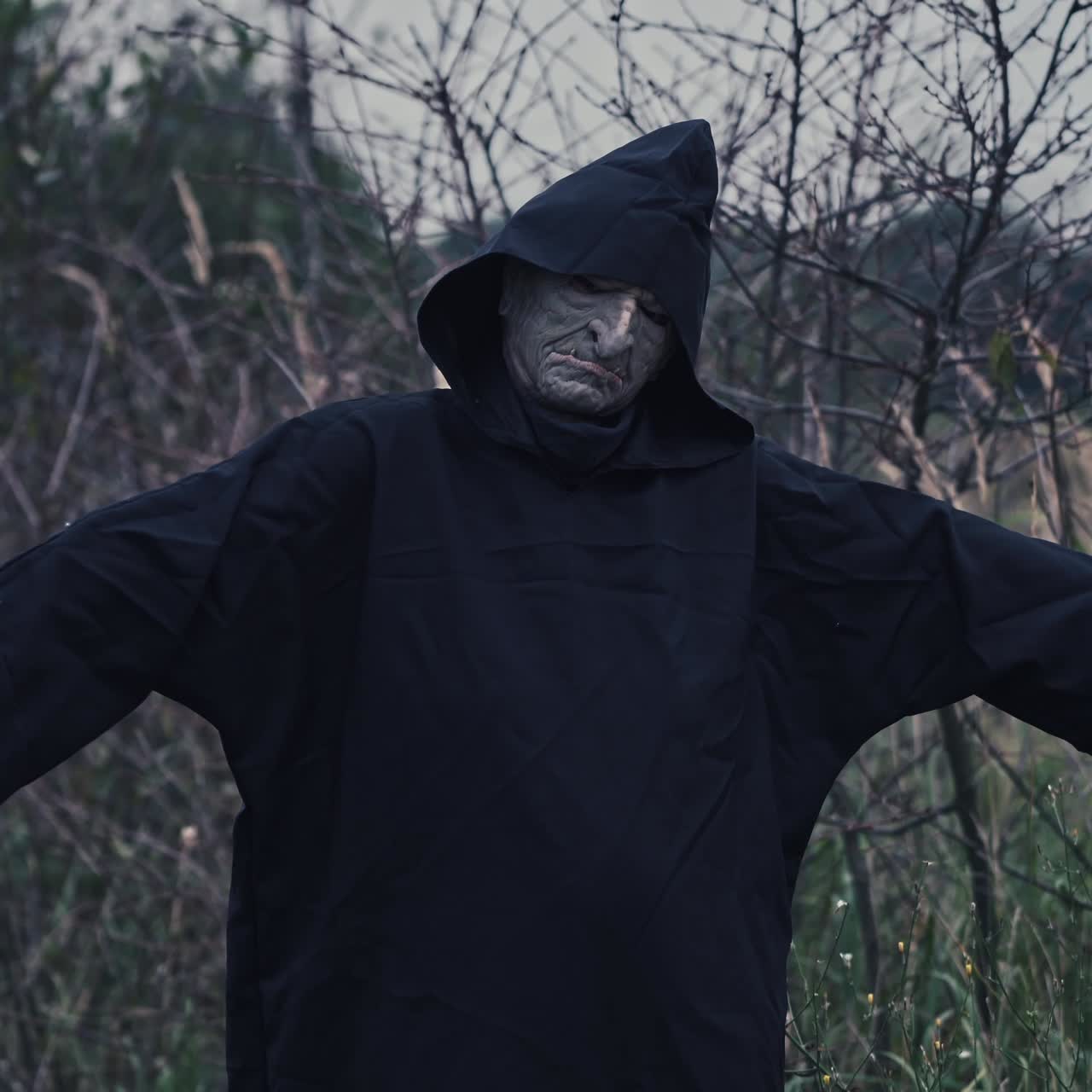 Portrait of terrible ghost outdoors. Scary figure of evil in black costume standing in nature with outstretched arms. Concept of horror.