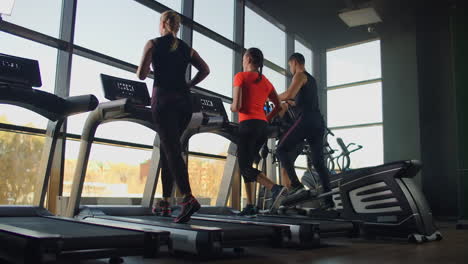 a group of people running on treadmills near a large panoramic window. group cardio workout