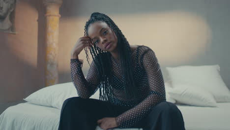 dark skinned girl posing by sitting on bed