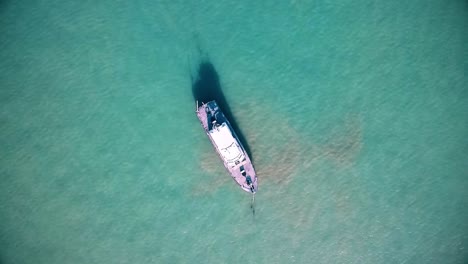 experimente una impresionante vista de pájaro mientras un dron captura un gran barco que se desliza a través del mar translúcido, revelando impresionantes detalles submarinos.