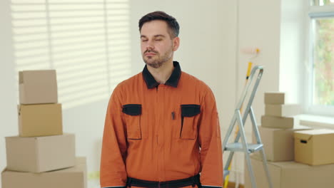 smiling worker in orange jumpsuit in a room with boxes and ladder