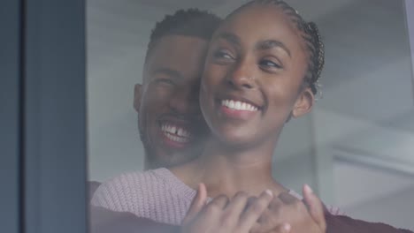 Close-up-of-happy-african-american-couple-standing-at-window-and-hugging