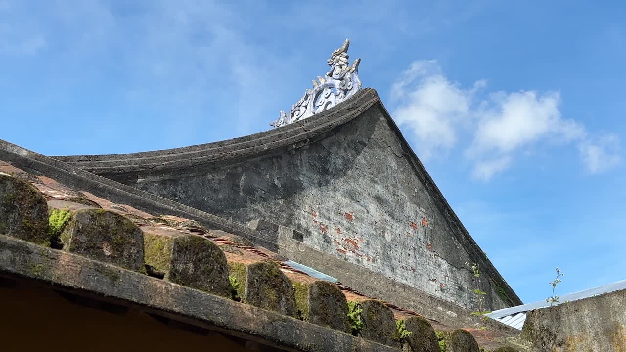 techo inclinado del templo con pieza central cultural en el ápice y musgo en hoi an, vietnam ciudad antigua con fondo de cielo azul