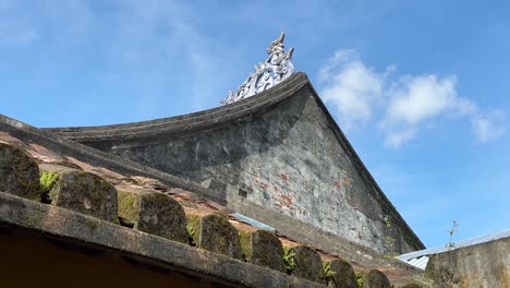 temple pitched roof with cultural centrepiece on apex and moss in hoi an, vietnam ancient town with blue sky background