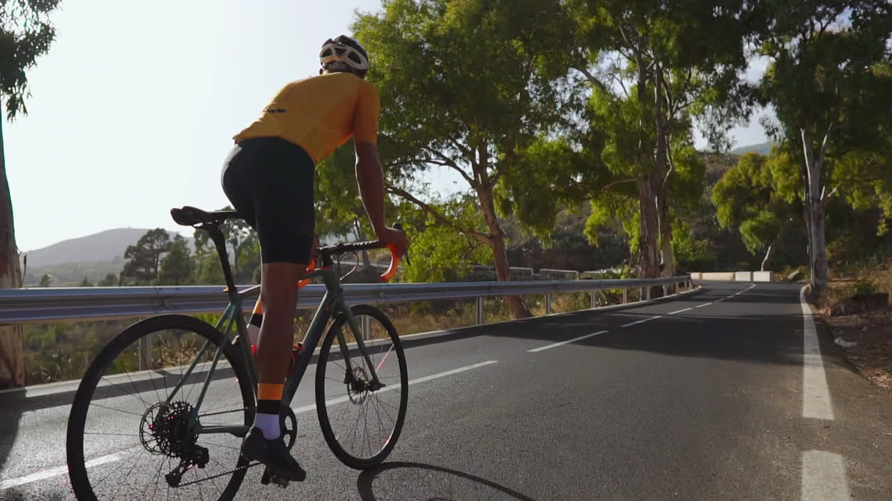 With the backdrop of a calm morning, a man cycles on his road bike on an empty road as part of outdoor exercise. The slow-motion capture accentuates the extreme sports vibe