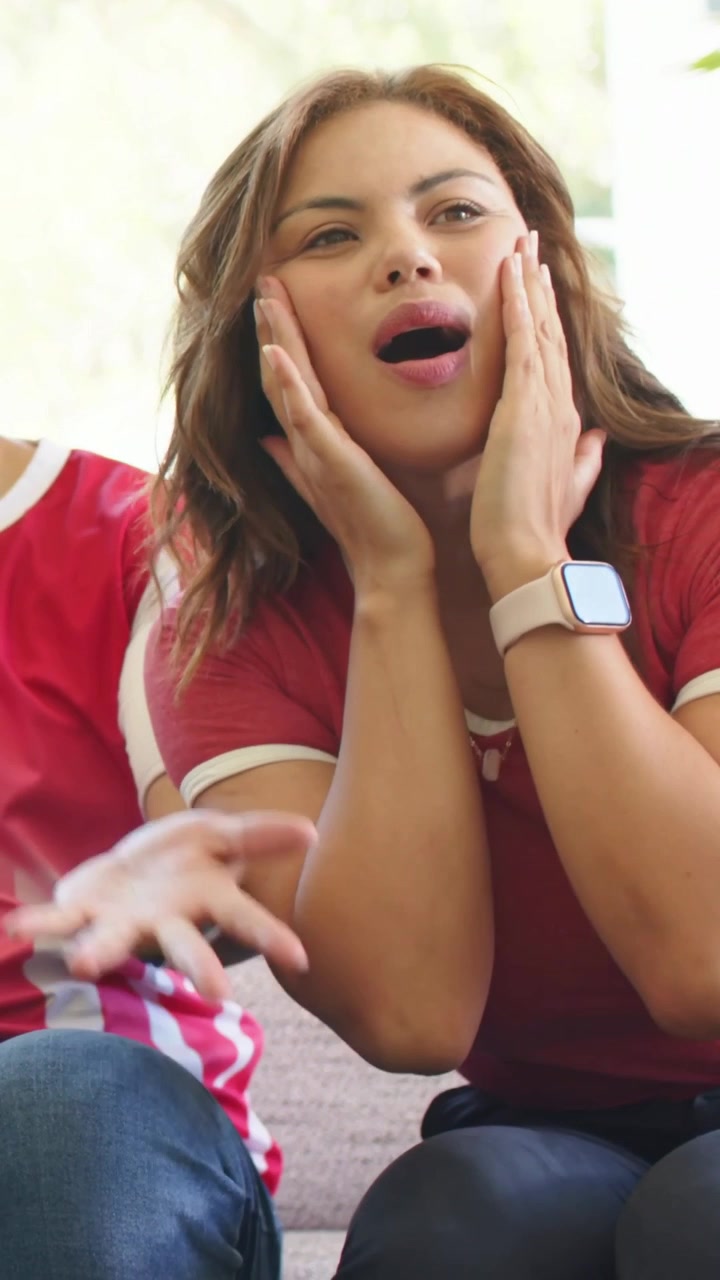 Vertical video: Woman reacting to off-screen sports play, leaning, cupping face, cheering with man