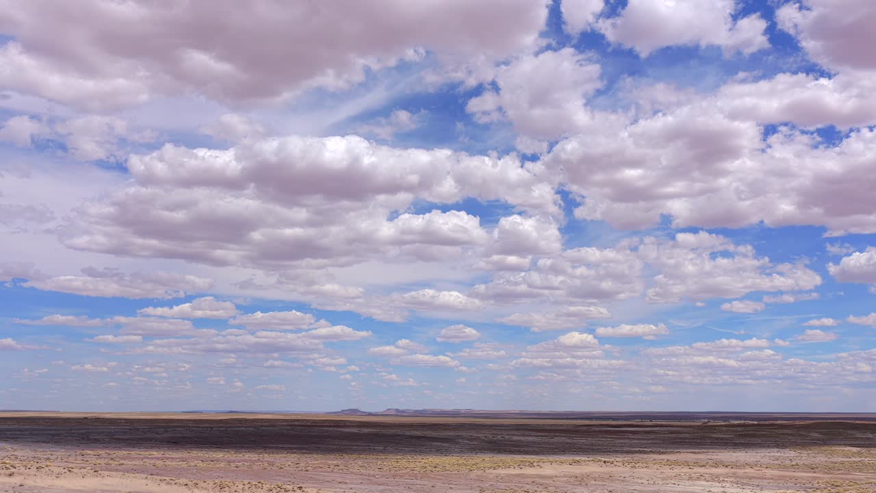 En filmisk drönartimelapse fångar vita moln som rör sig snabbt över en blå himmel över ett vidsträckt ökenlandskap i Arizona. Denna film framhäver det dynamiska vädret och omfattningen av sydvästra USA.