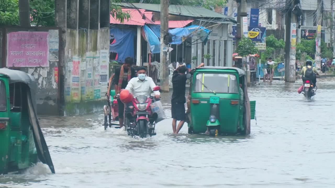 CNG, cars, motorcycle, and rickshaw drive through flooded street in Sylhet, Bangladesh