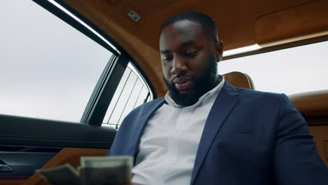 portrait of businessman counting money at car. african guy smelling money at car