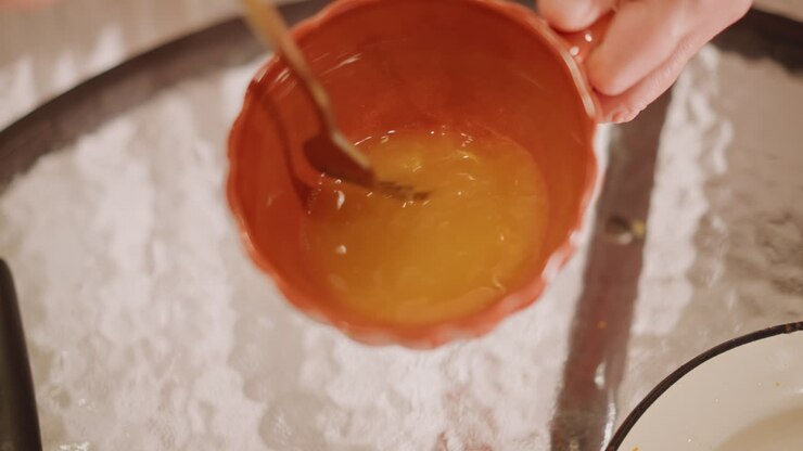 Shiny pumpkin glaze in small mixing bowl. Kitchen scene showcasing seasonal pumpkin glaze application. Closeup view of smooth pumpkin glaze being stirred for festive pie decoration