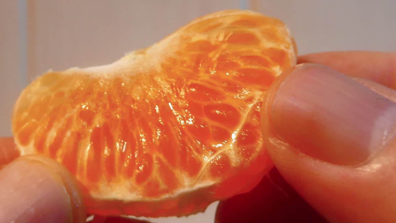 Primo piano di dita che spremono uno spicchio di mandarino fresco, rivelandone la polpa succosa e la consistenza.