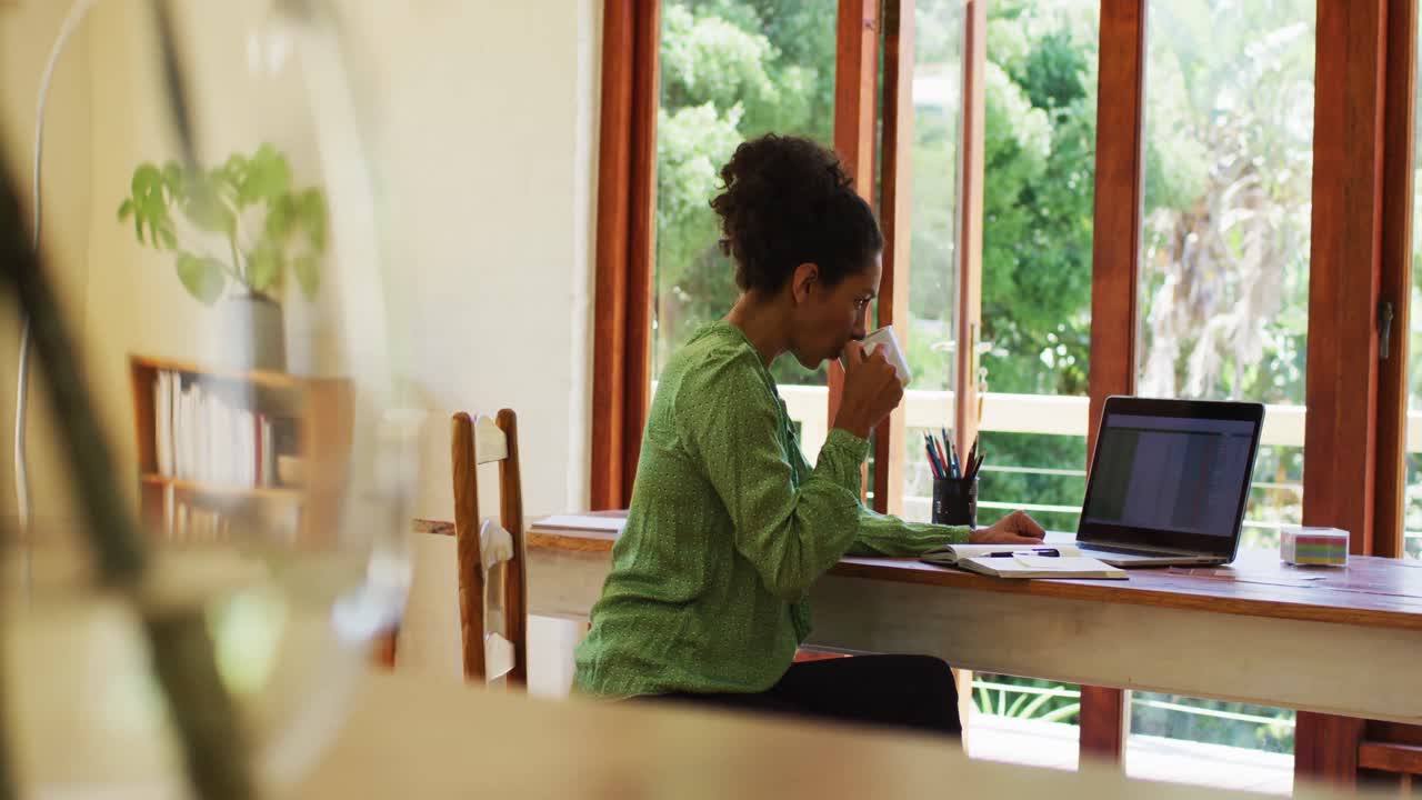 Mixed race woman drinking coffee and working from home