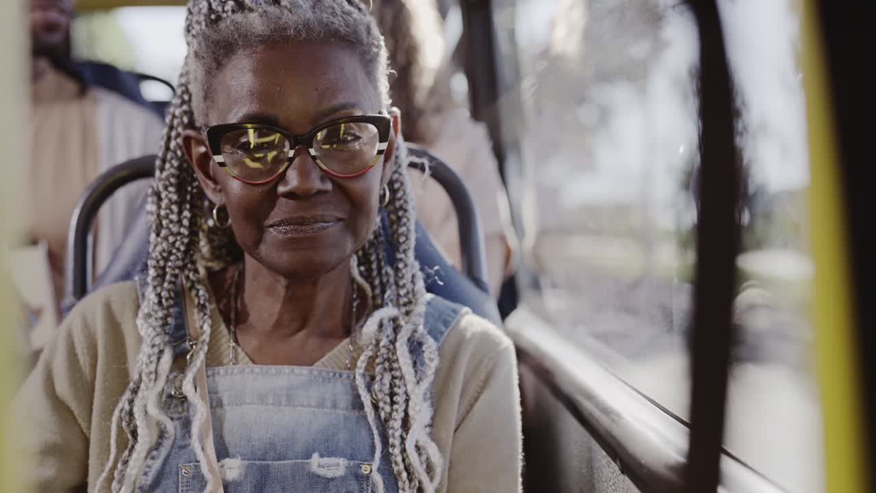 Close-up portrait of an older African American woman with braided hair and glasses smiling on a bus