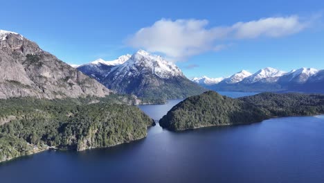 panoramic view of a serene lake surrounded by snow-capped mountains and forests
